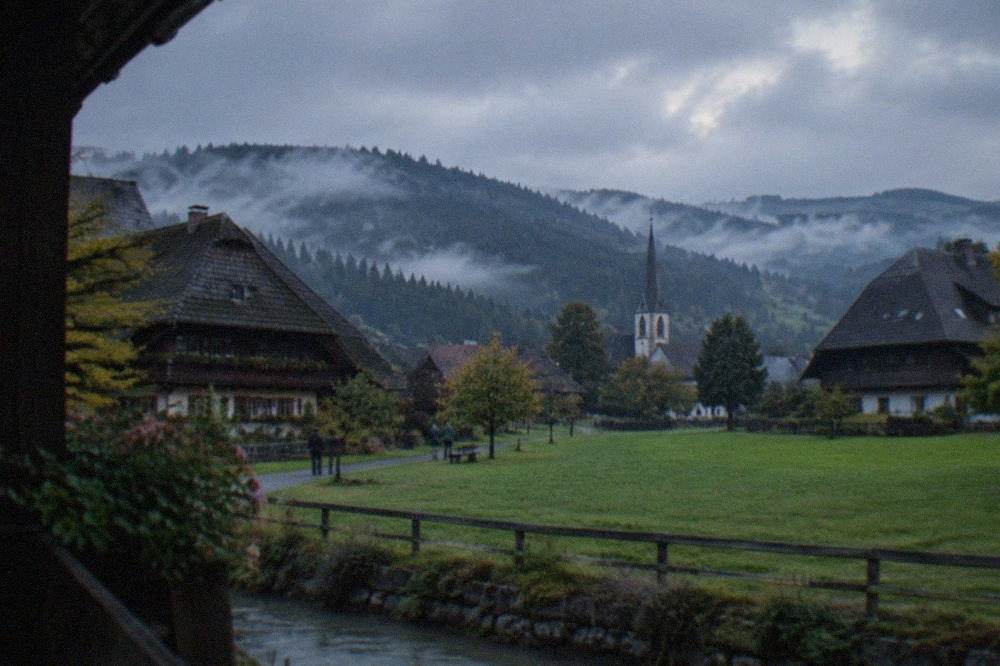 Morning mist over dark forested hills with a small village church spire in a valley