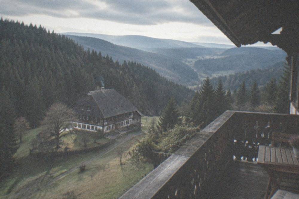 A traditional Black Forest guesthouse balcony with carved wooden railings facing forest hills