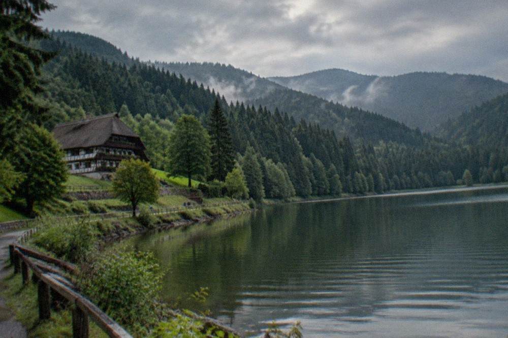 A calm mountain lake ringed by dark fir forest with a small promenade along the shore