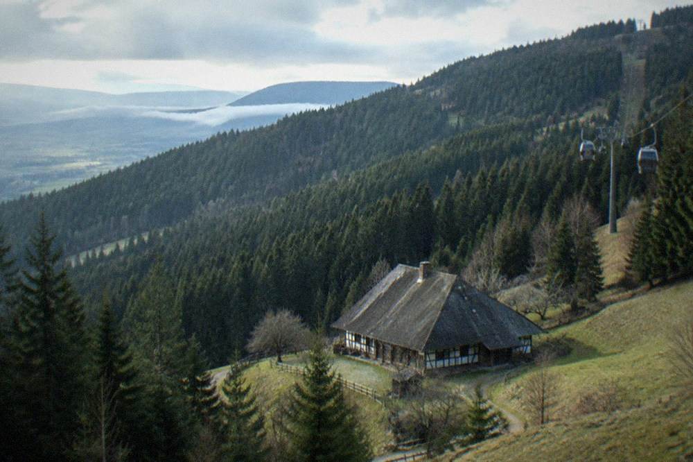 Cable car cabins ascending forested slopes toward the Schauinsland summit above cloud lines