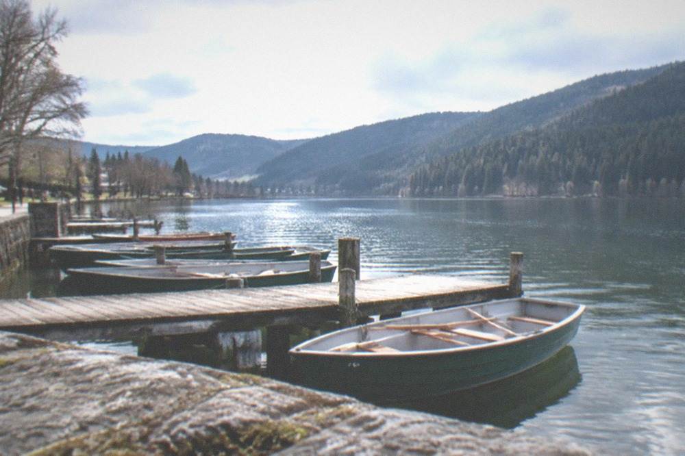Lake Titisee with forested mountains behind a calm shoreline and moored boats