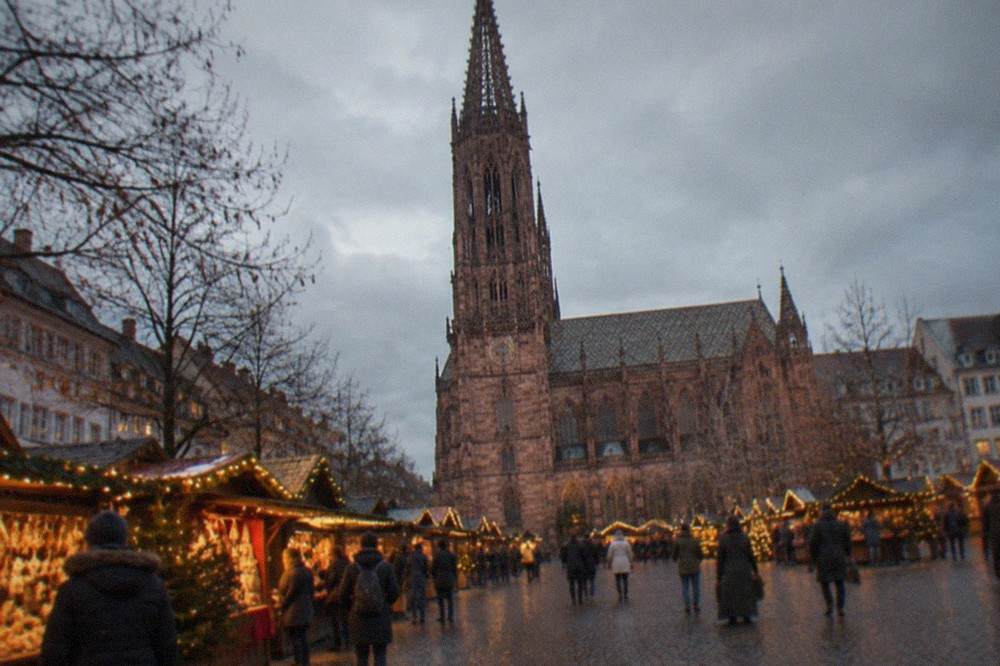 Illuminated Christmas market stalls on a Freiburg square at dusk with warm string lights