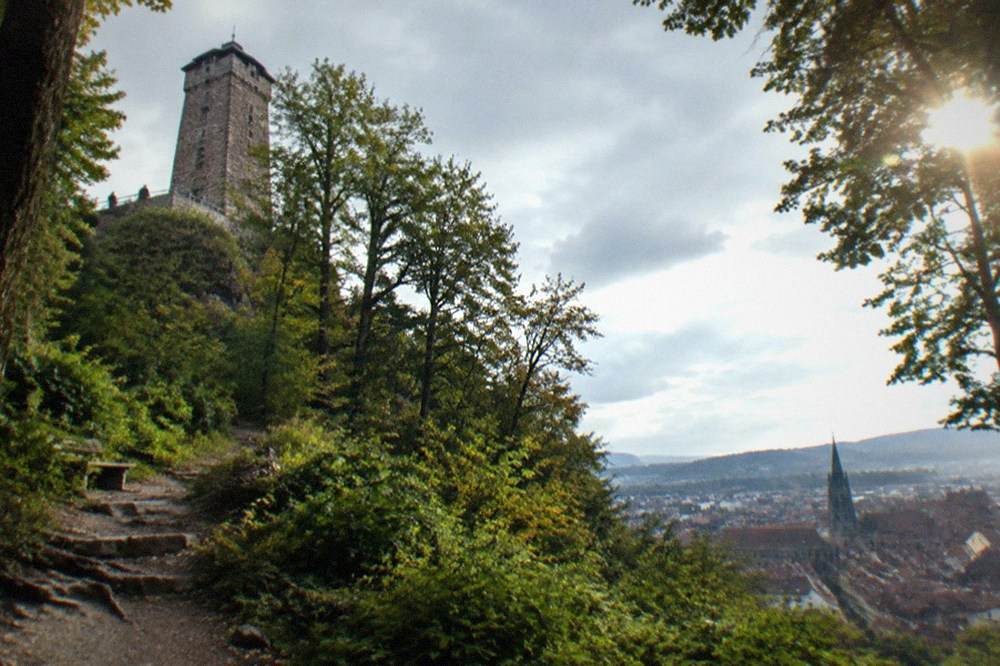 A stone lookout tower on the Schlossberg above a wooded hillside with the city below