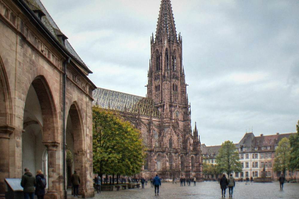Interior courtyard of a Freiburg museum with high stone arches and visitors reading displays