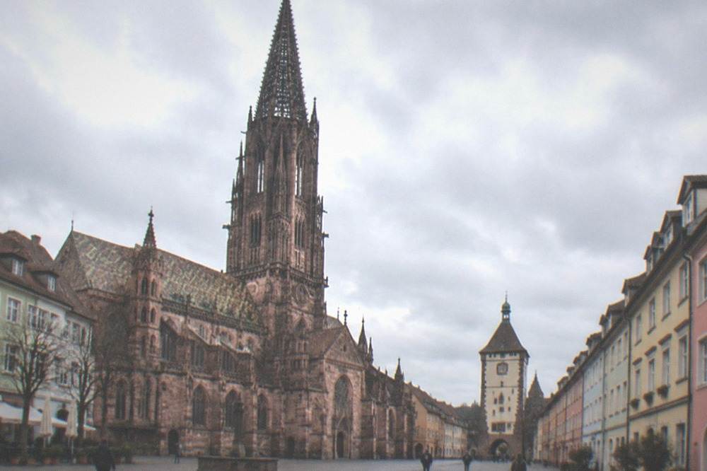 Quiet old town street in Freiburg with pastel facades and a view toward a city gate tower
